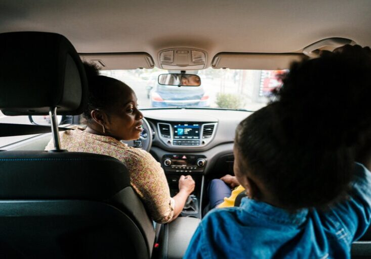 Back view of content African American girl with parents driving car together during road trip through city and sharing news to each other